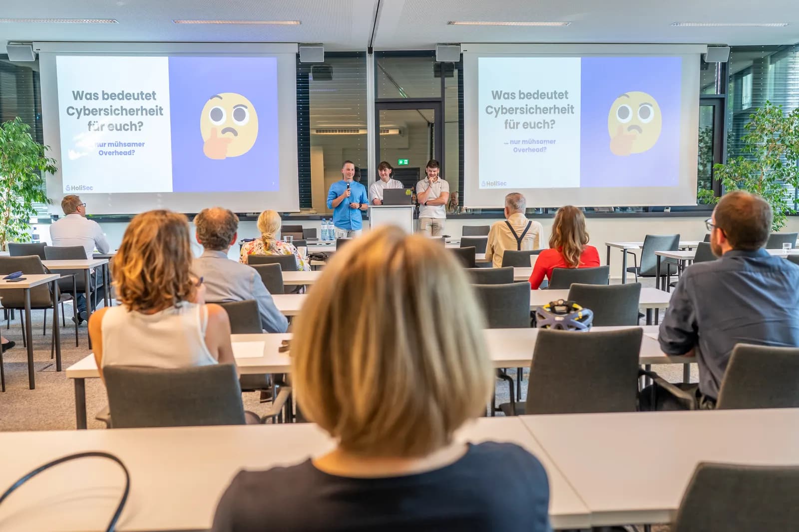 Blick über das Publikum beim Cyber Security Awareness Training der KSW; auf zwei Leinwänden die Frage „Was bedeutet Cybersicherheit für euch?“
