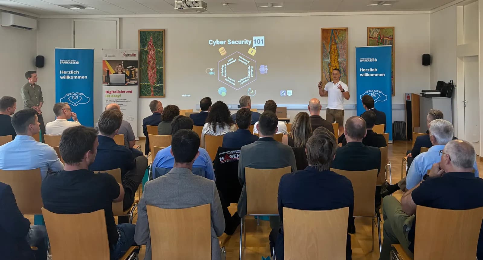 Vortrag „Cyber Security 101“ in Leibnitz: ein HoliSec-Gründer spricht vor voll besetztem Saal, auf der Leinwand die Titelfolie